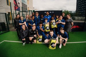 The full squad of young players and coaches posing together on the pitch holding their JD Sports bags and gift cards